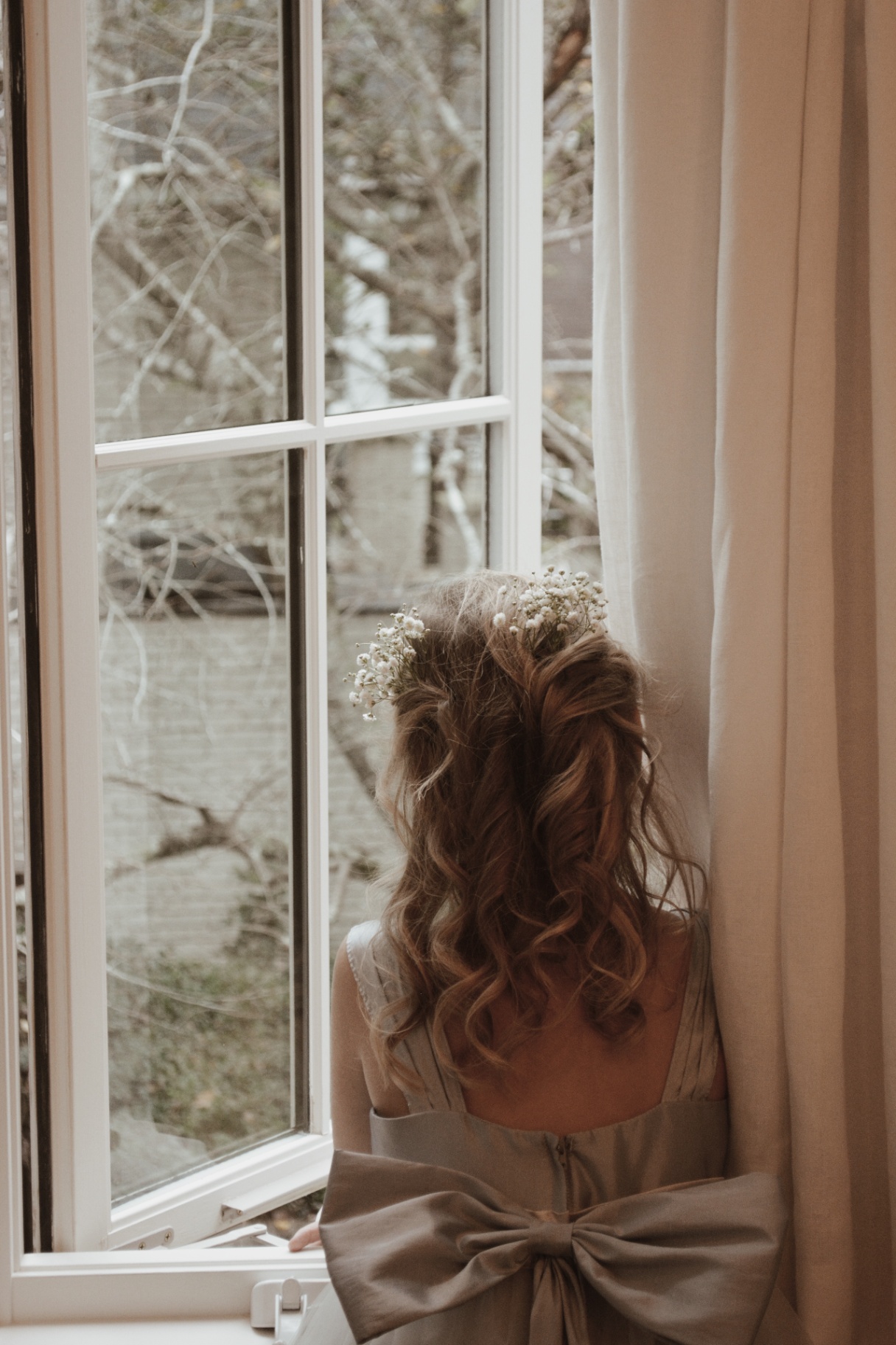 Bride by a window with bow detail on the back of her dress